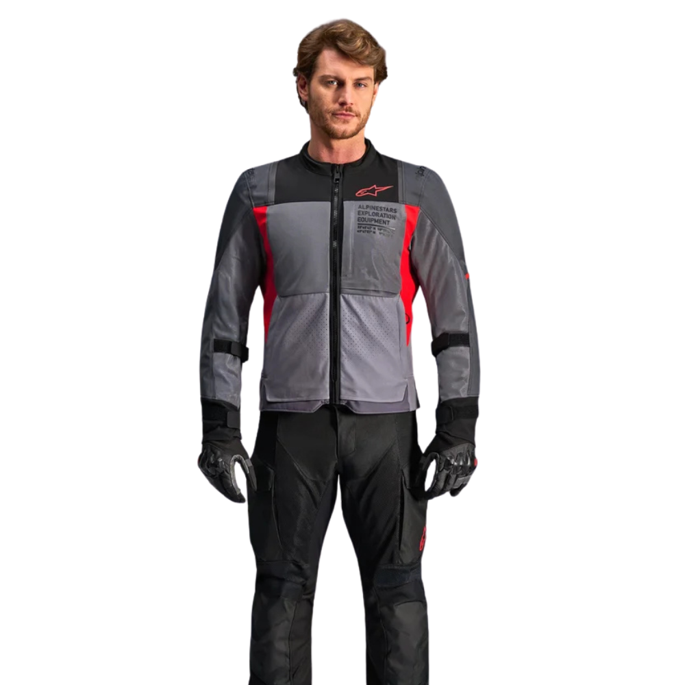 A man modeling a gray and black Alpinestars motorcycle jacket with red accents, paired with black pants and gloves, against a plain white background.