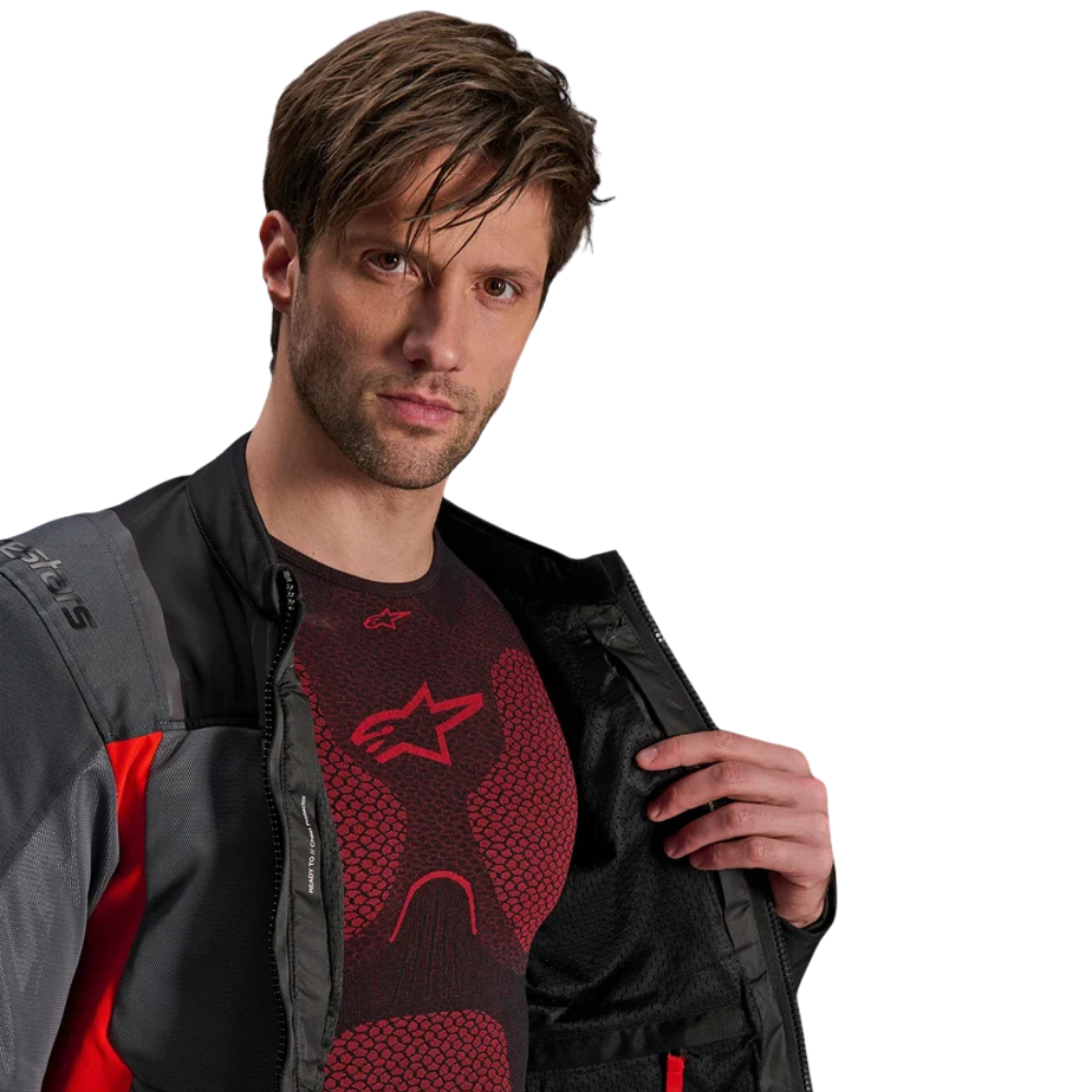 A man wearing a black and gray Alpinestars motorcycle jacket over a red and black Alpinestars compression shirt, shown against a solid white background.
