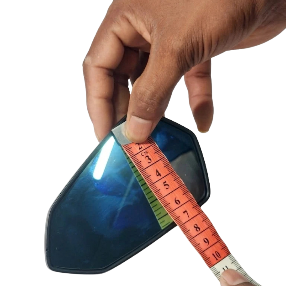 A hand holding a blue-tinted lens or visor while measuring it with a red tape measure against a plain white background.