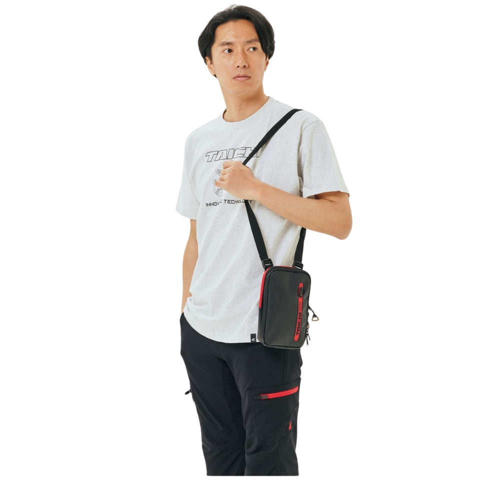 Person wearing a white t-shirt and black pants holding a black crossbody bag with red accents on a white background