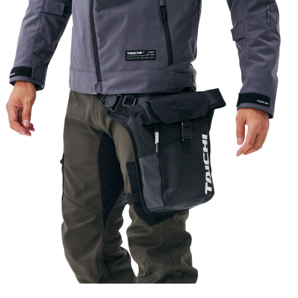 Person wearing a gray jacket and black bag with 'Tachi' branding on a white background